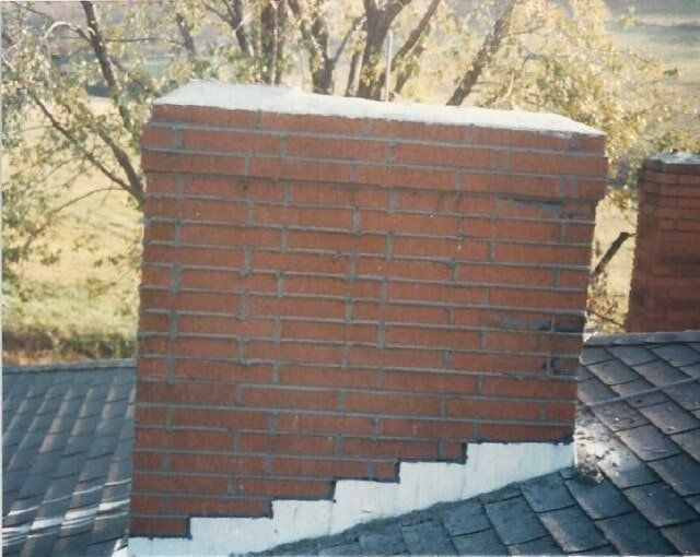 A red brick chimney on a shingled roof with white flashing along the base.