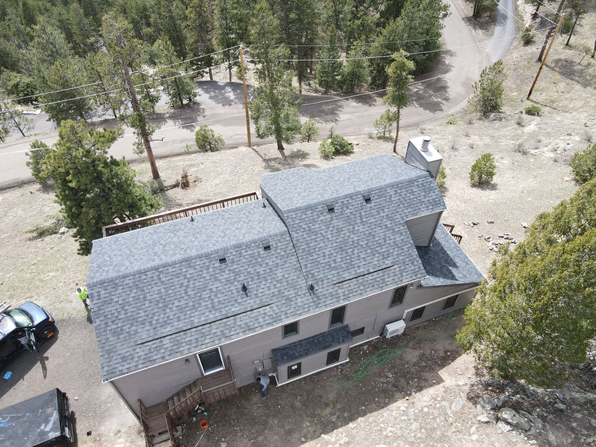 An aerial view of a house with a roof in the middle of a forest.
