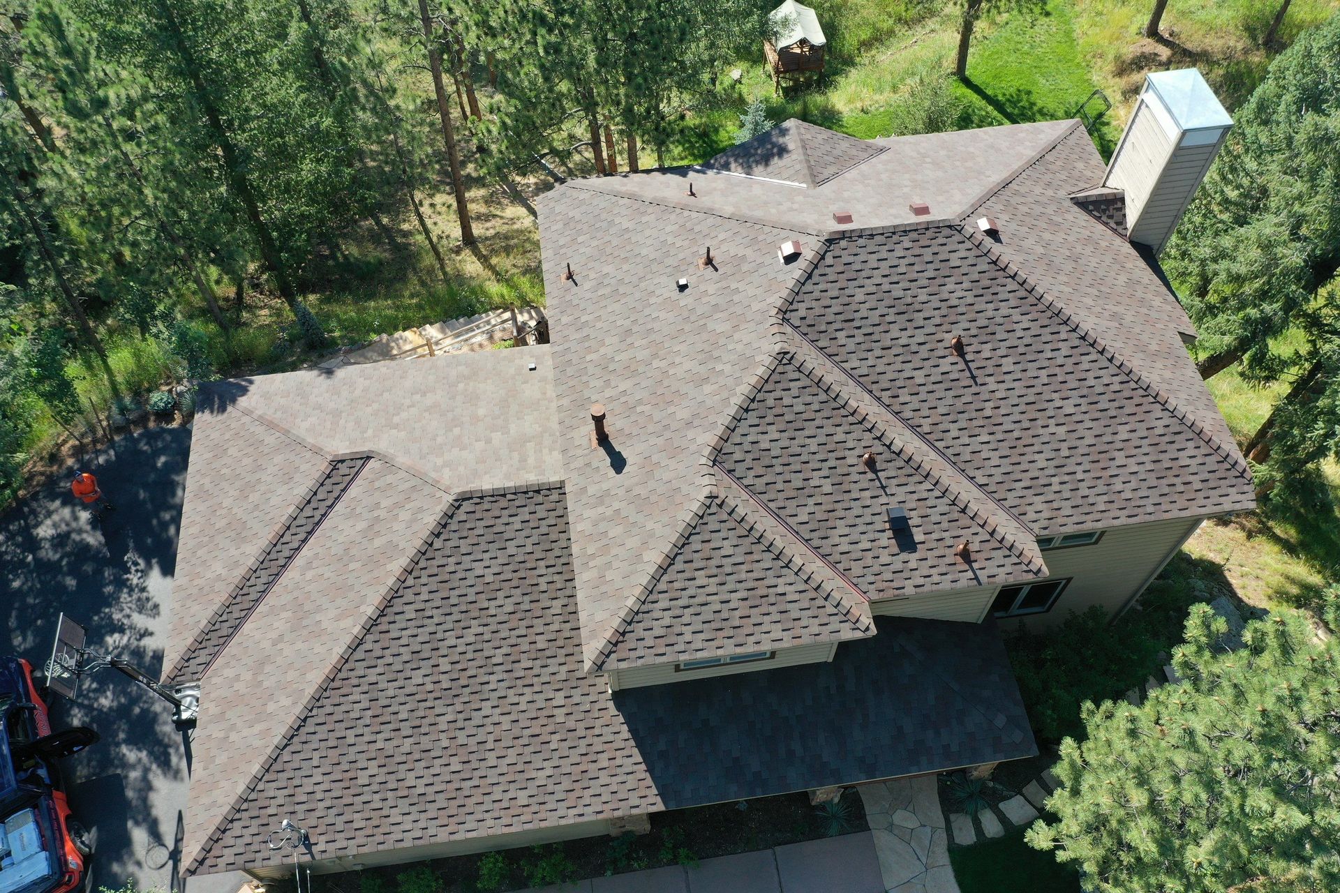 An aerial view of a house with a roof that is surrounded by trees.