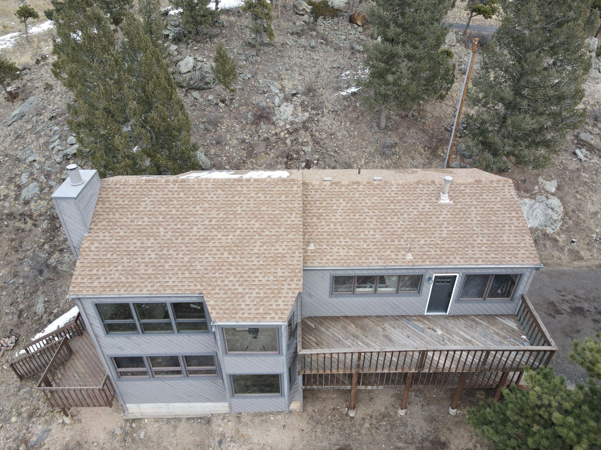 An aerial view of a house with a deck in the middle of a forest.