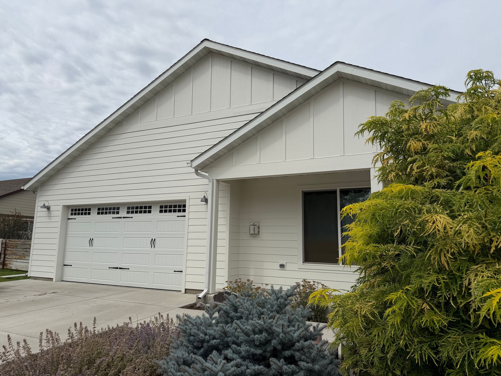 Single-story white suburban house with a two-car garage and front yard shrubs