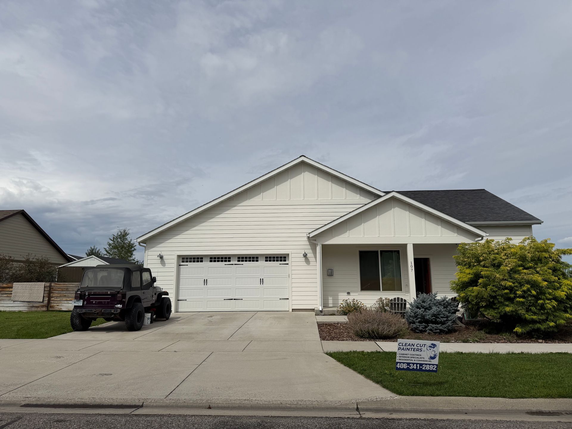 Suburban single-story house with attached garage, driveway, and front lawn under a cloudy sky