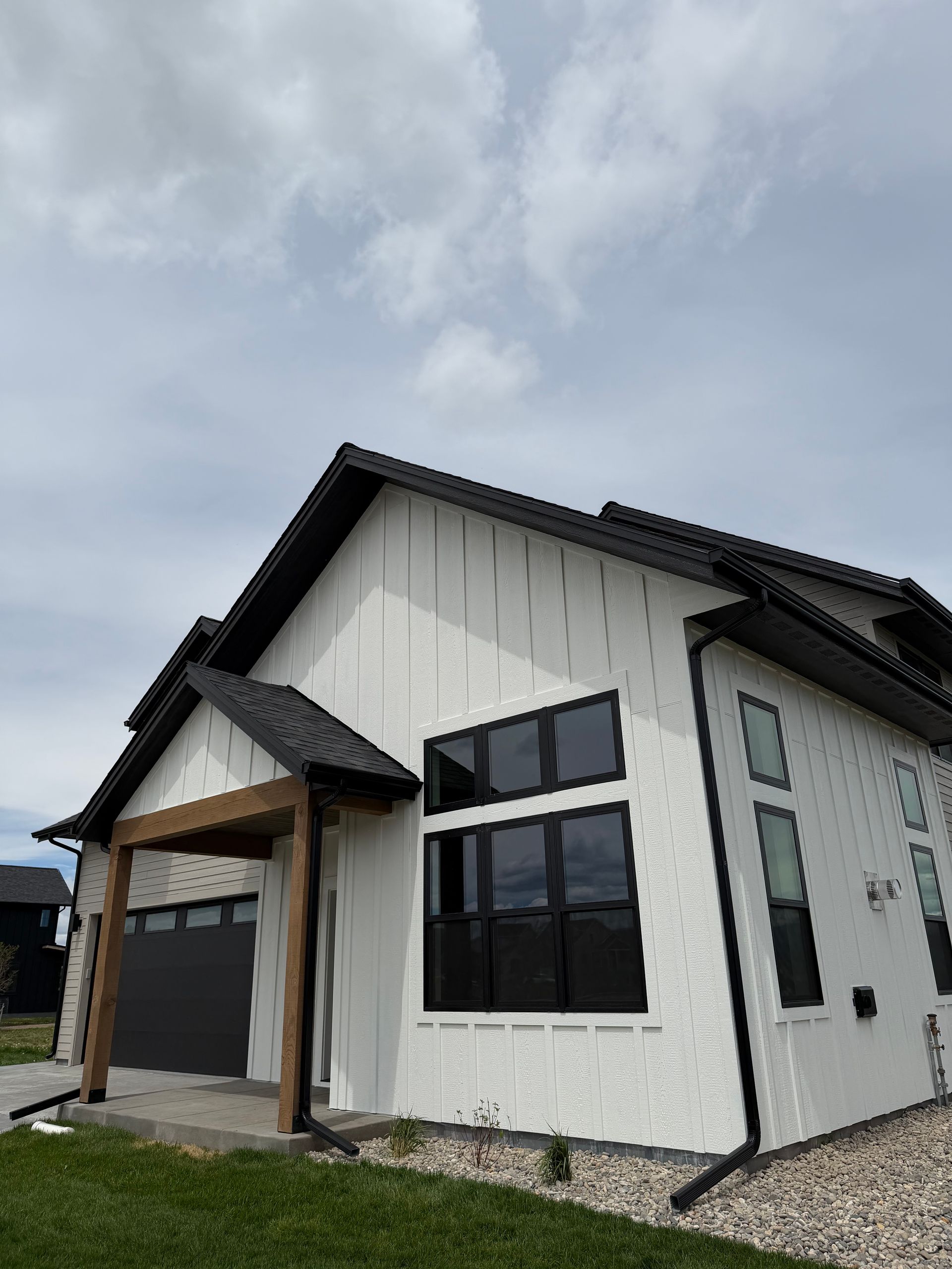 Modern white house exterior with black trim, garage, and gravel landscaping under a cloudy sky
