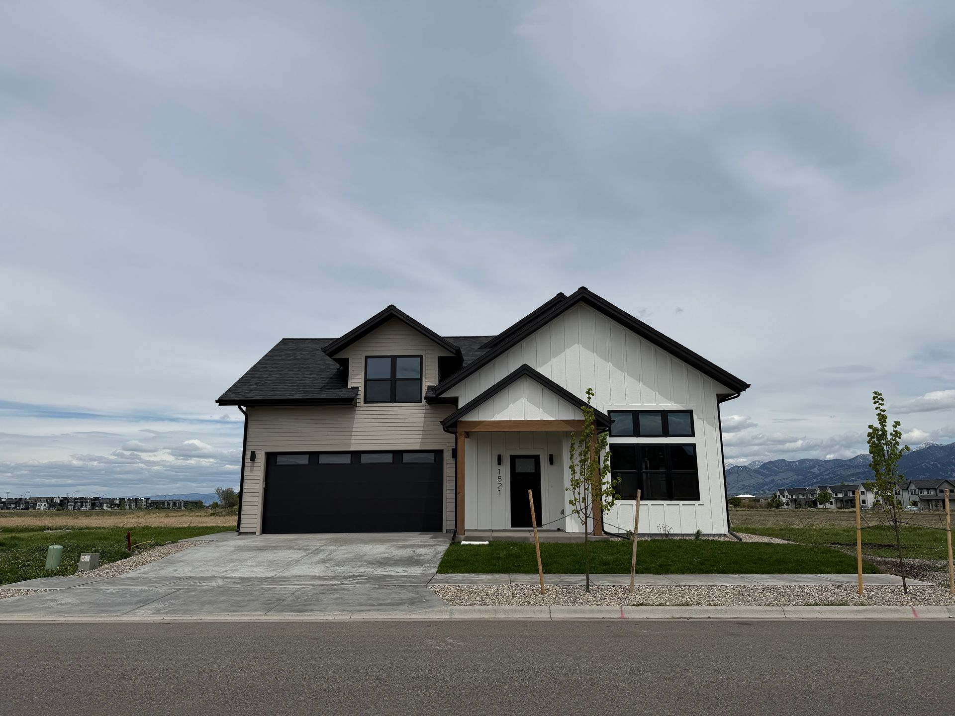 Modern two-story house with dark roof, large driveway, and small front lawn under a cloudy sky