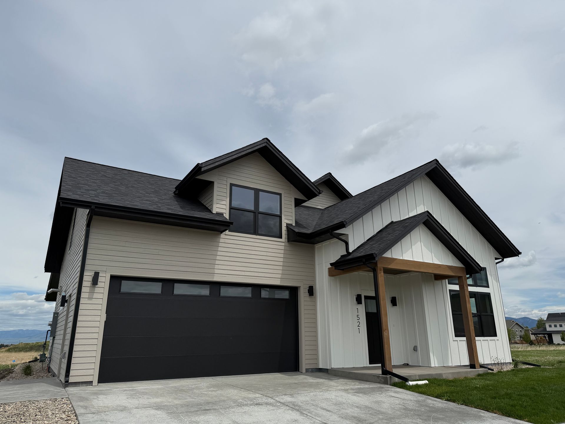 Modern two-story house with black garage door and white siding under a cloudy sky