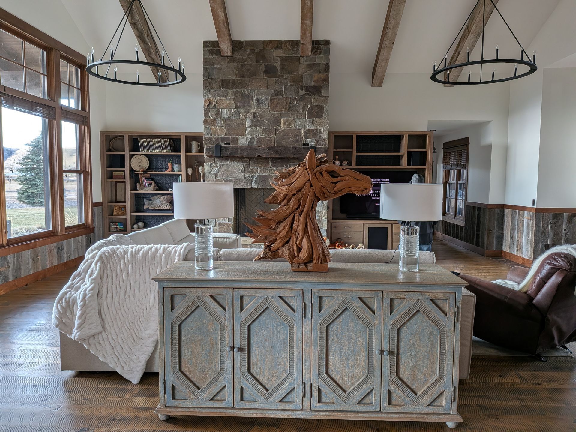 Rustic living room with stone fireplace, white sofa, patterned console, and wood-beam ceiling