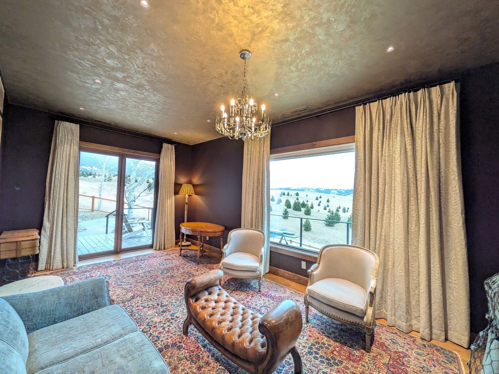 A luxurious, moody living room with dark purple walls, a patterned rug, velvet furniture, and expansive window views.