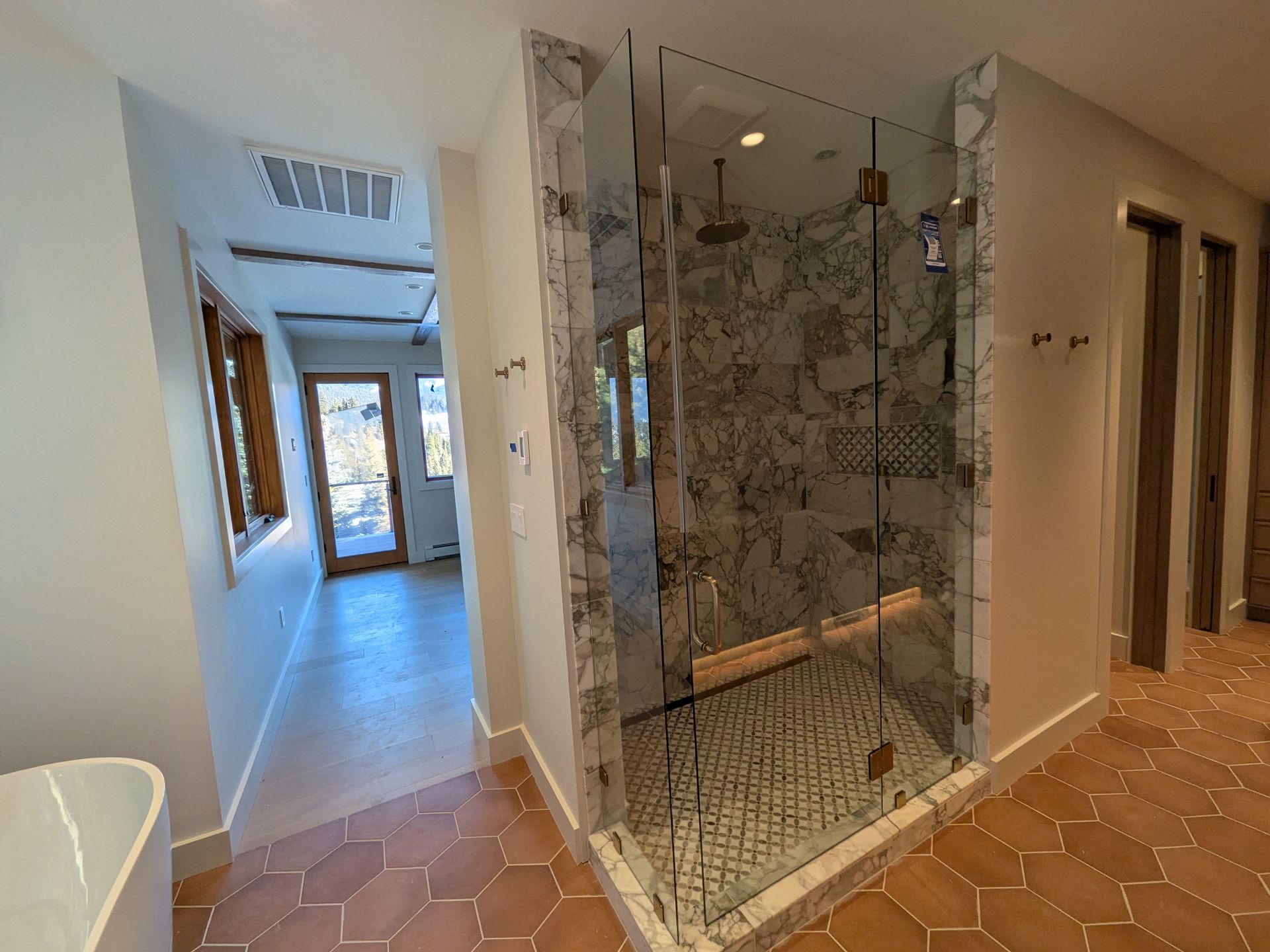 Hallway with a glass-enclosed shower and terracotta tile floor in a modern interior