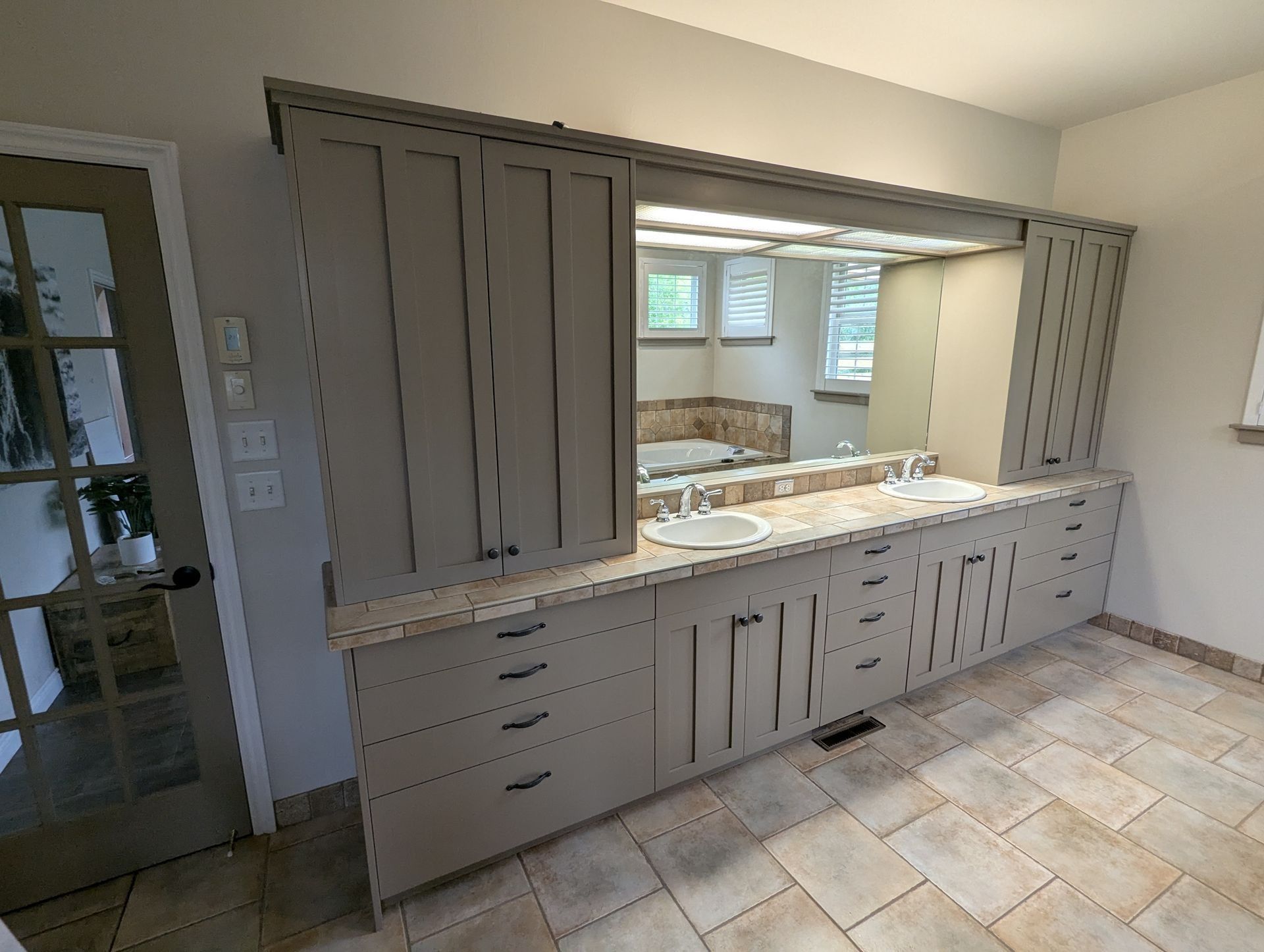 A double bathroom vanity with beige cabinets, stone countertops, two sinks, and a large mirror in a tiled room.