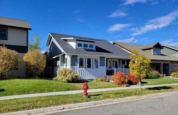 A two-story blue and white house with solar panels on a sunny, tree-lined street with a red fire hydrant in the front.