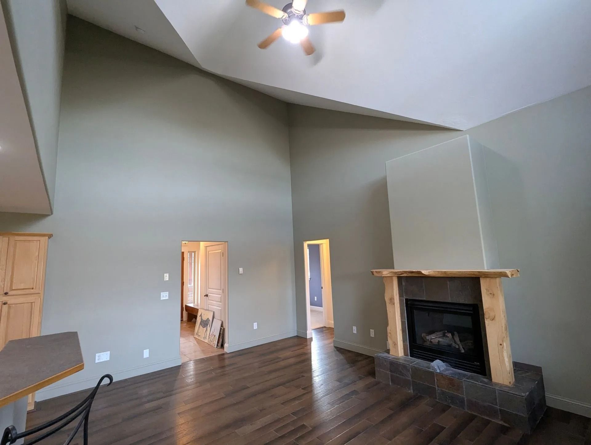 A spacious room with high vaulted ceilings, hardwood floors, a stone fireplace with a wood mantel, and two doorways.