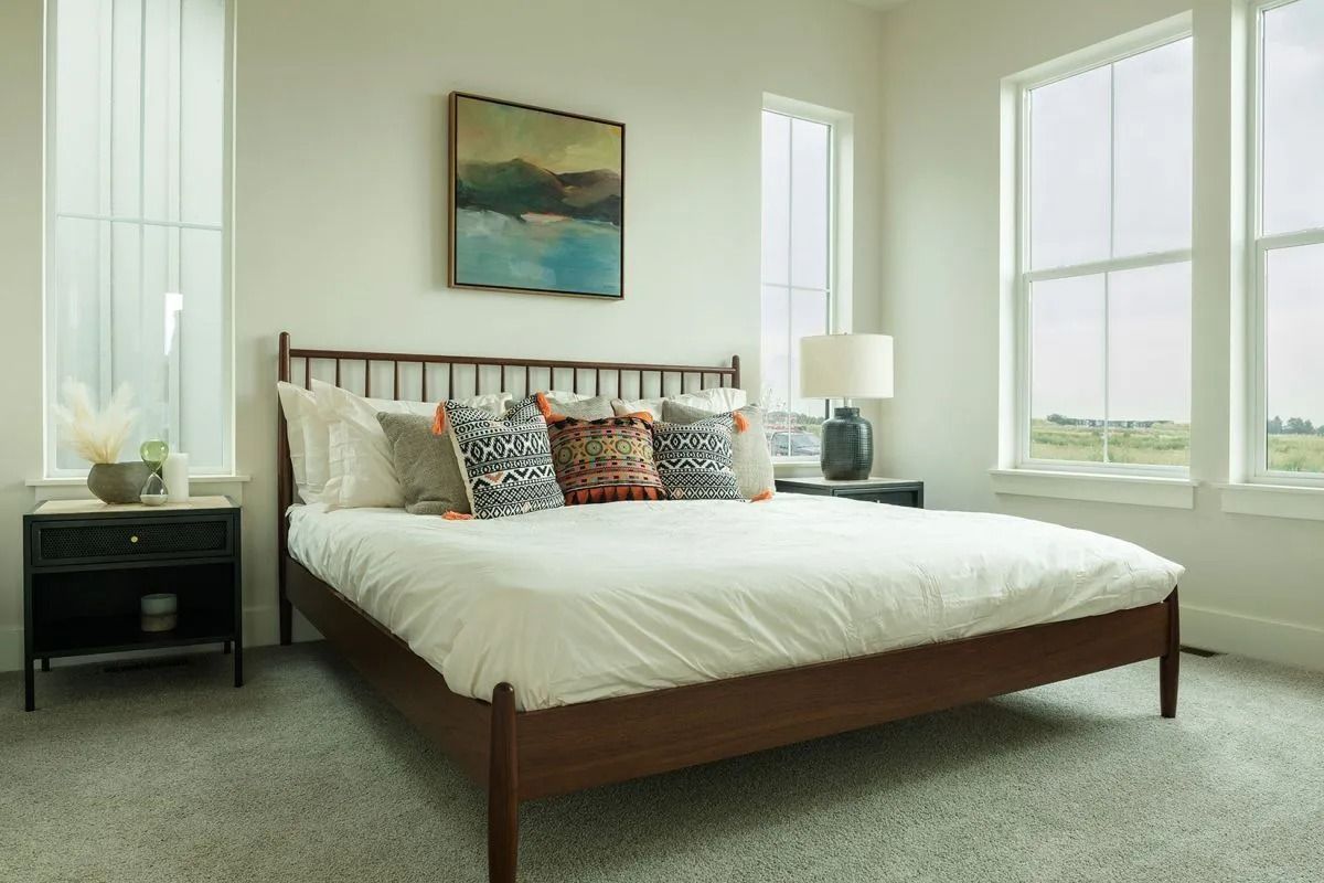 A neutral-toned bedroom features a dark wood bed with white bedding, patterned pillows, a side table, and wall art.