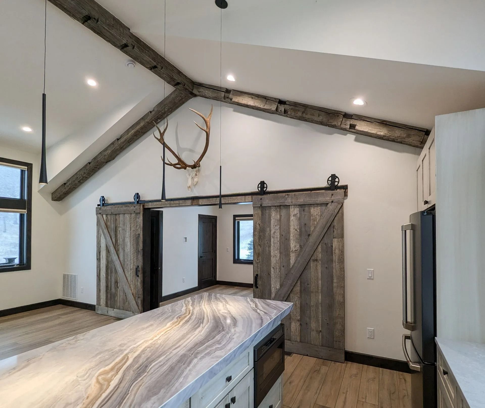 A kitchen interior featuring a marbled island, rustic wooden barn doors, and large exposed ceiling beams.