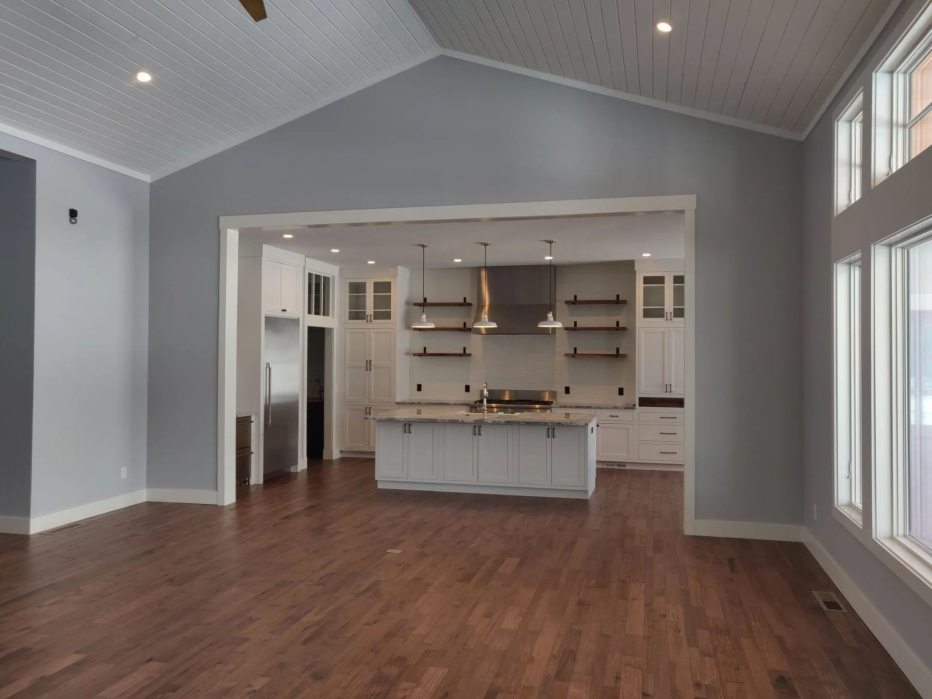 A spacious, modern open-concept kitchen and living area with hardwood floors, a white kitchen island, and vaulted ceiling.