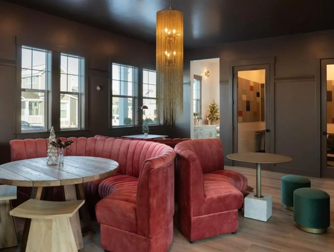 A modern lounge area with rounded, coral-colored velvet booths, light wooden tables, and a metallic chandelier.