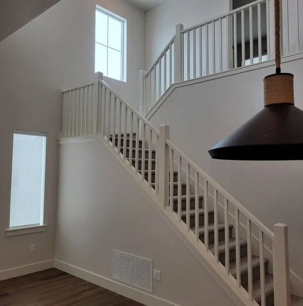 A modern staircase with white railings, beige carpeted steps, and wood flooring, illuminated by a large hanging light.
