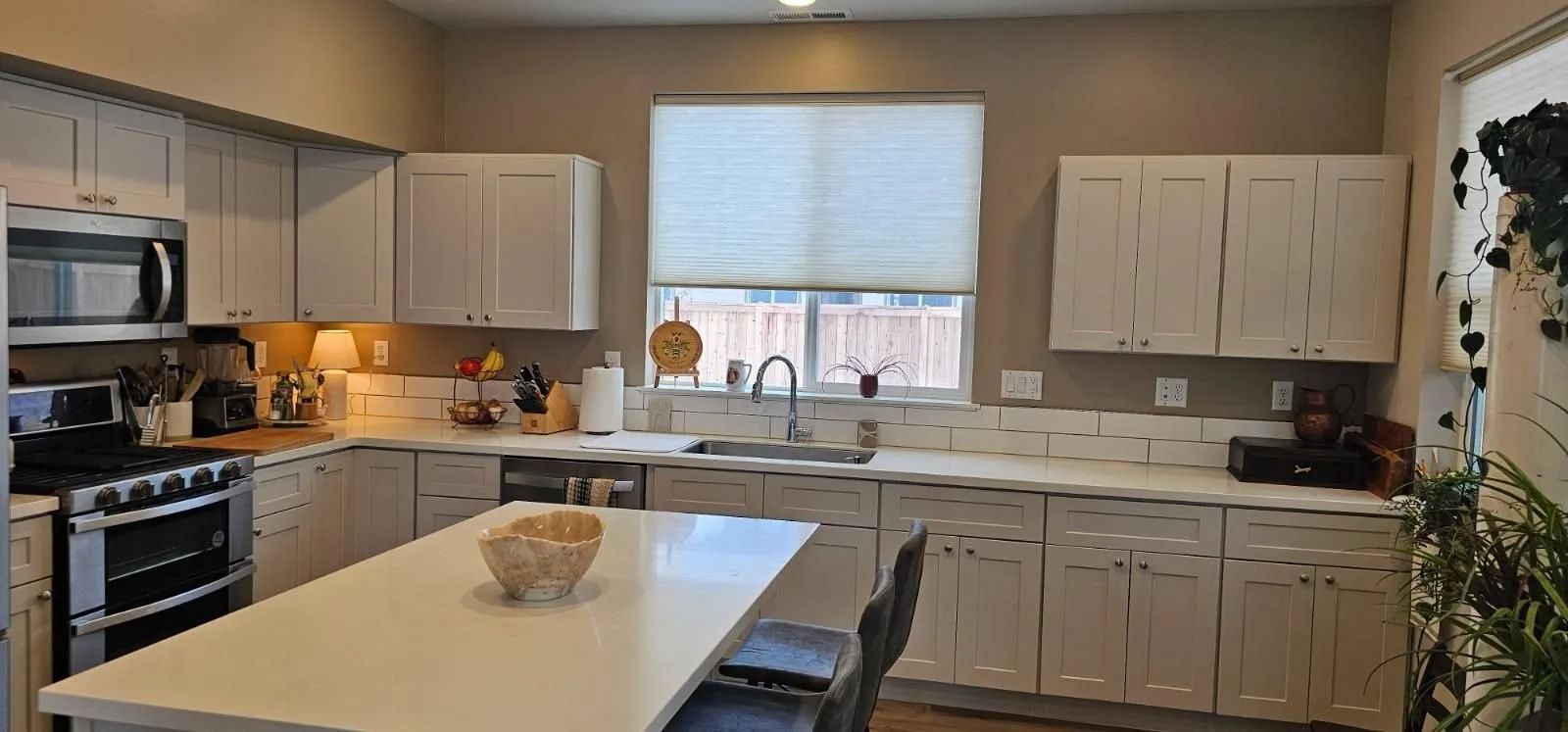 A bright, modern kitchen featuring white cabinets, stainless steel appliances, and a central island with two chairs.