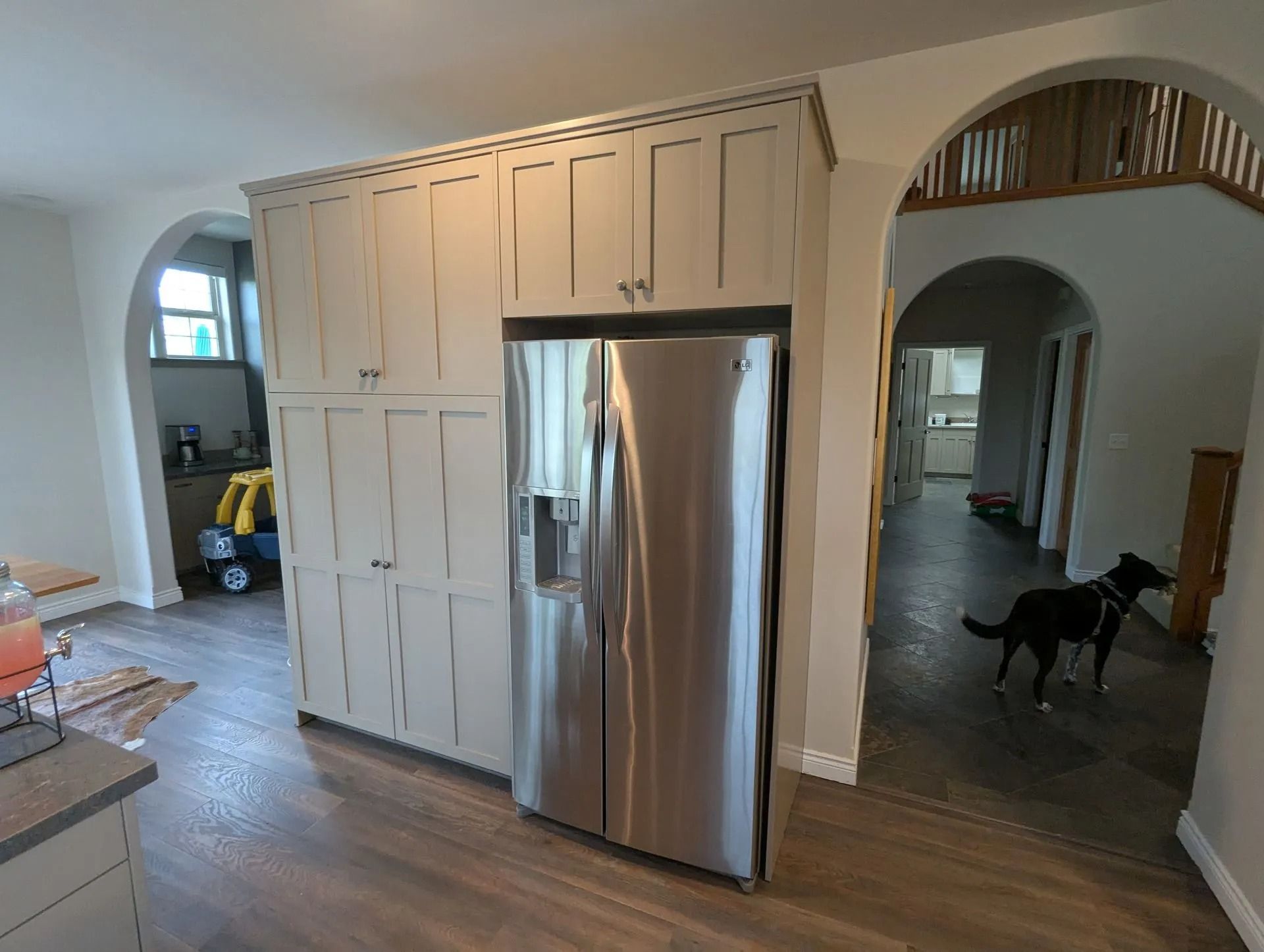 A stainless steel refrigerator is built into custom, light-colored cabinetry in a home with arched doorways and a black dog.