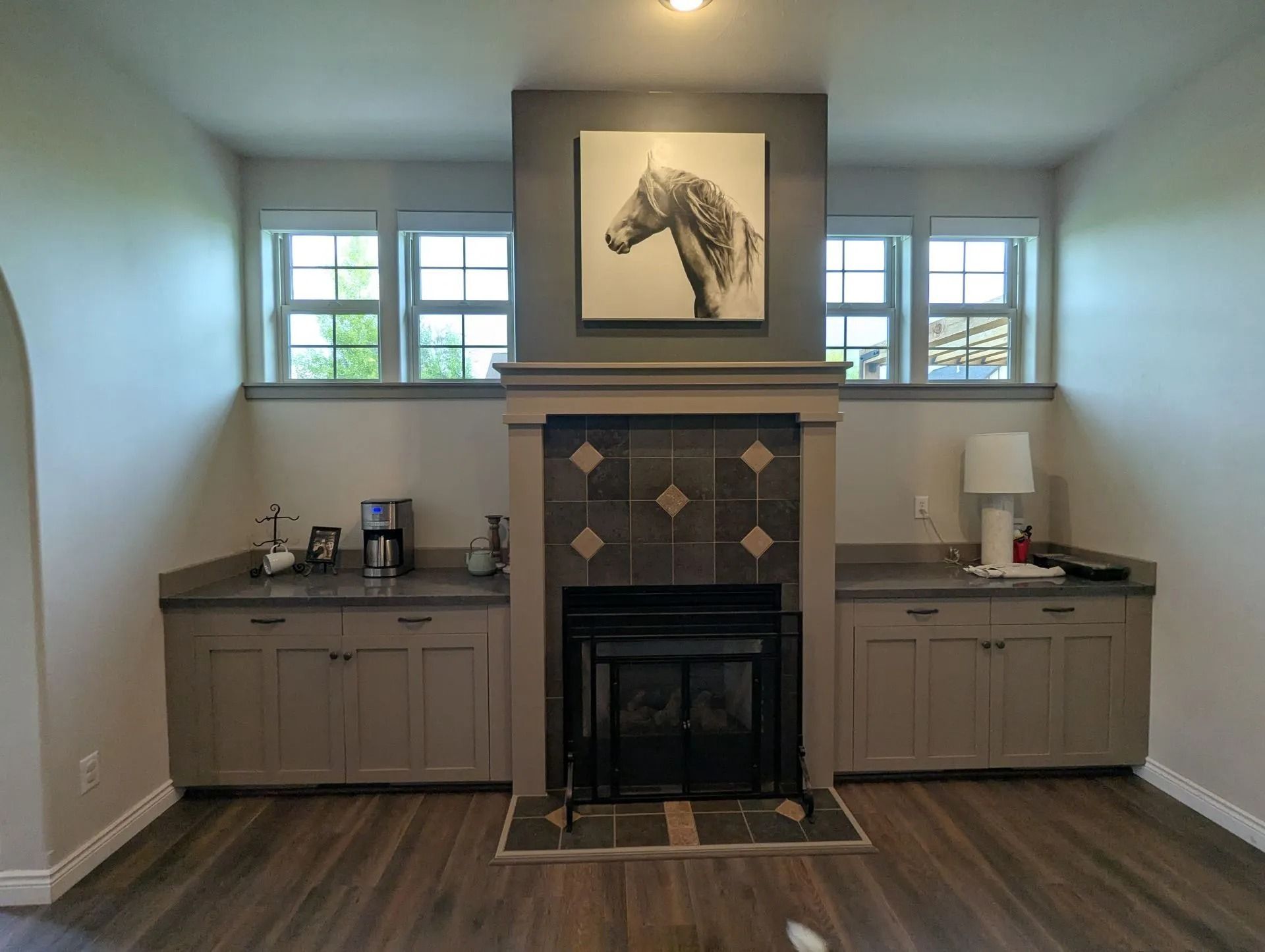 A neutral-toned room featuring a central fireplace with dark tile, flanked by matching cabinetry, windows, and decor.