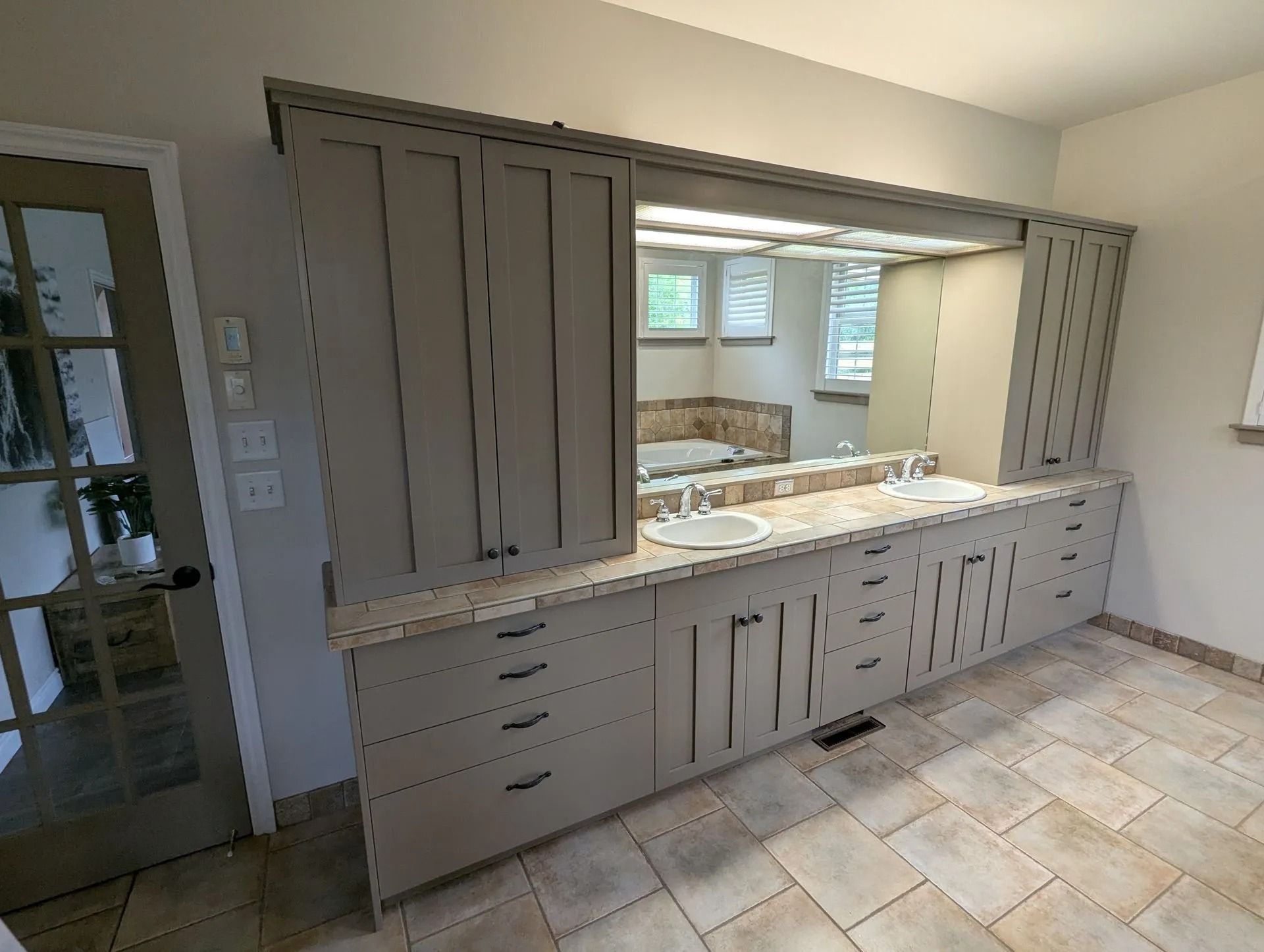 A grey bathroom vanity with a long mirror, dual sinks, and tall side cabinets, situated on a tiled floor.