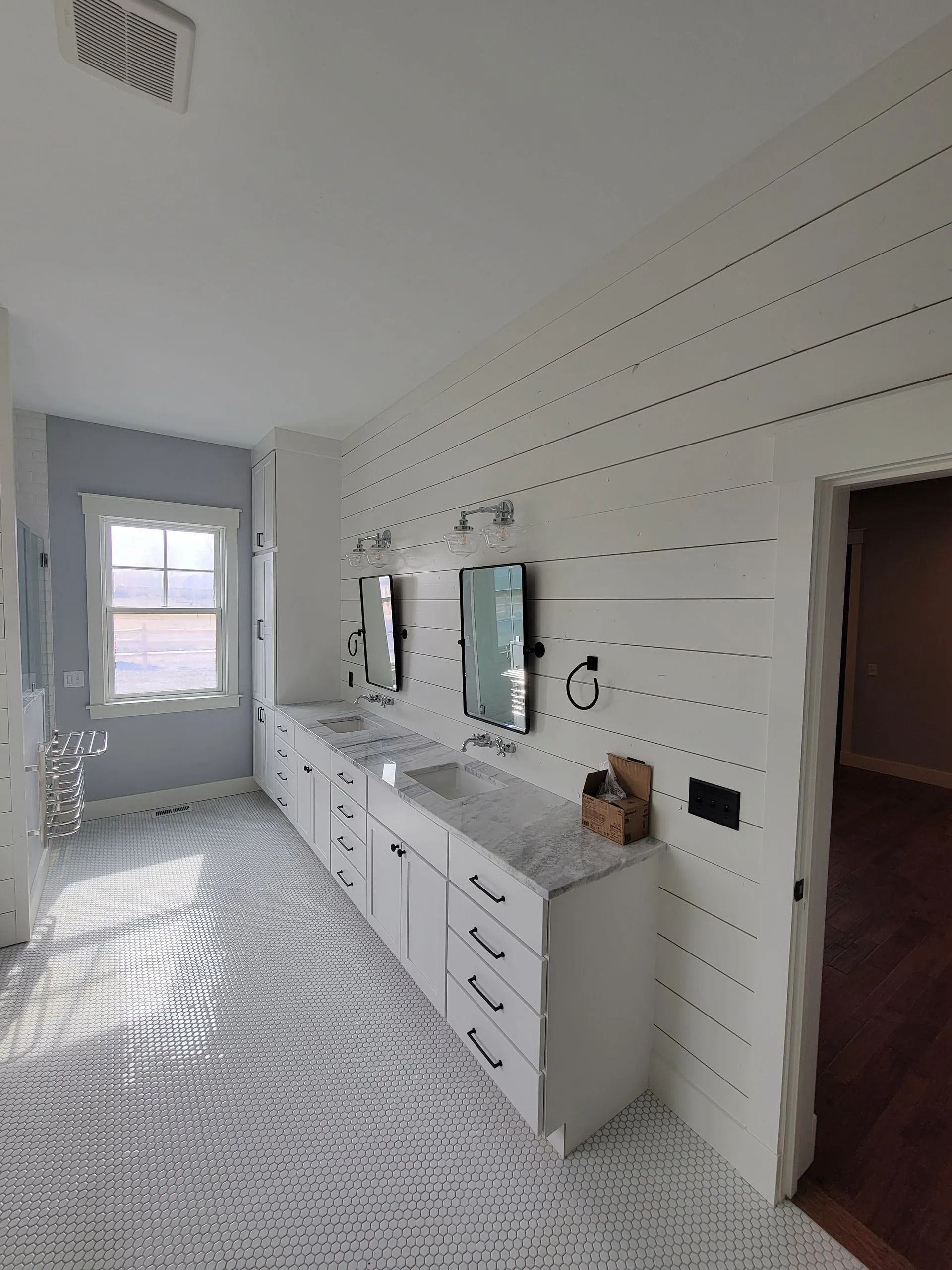 A modern bathroom featuring a white double vanity, shiplap wall, and intricate patterned tile floor.