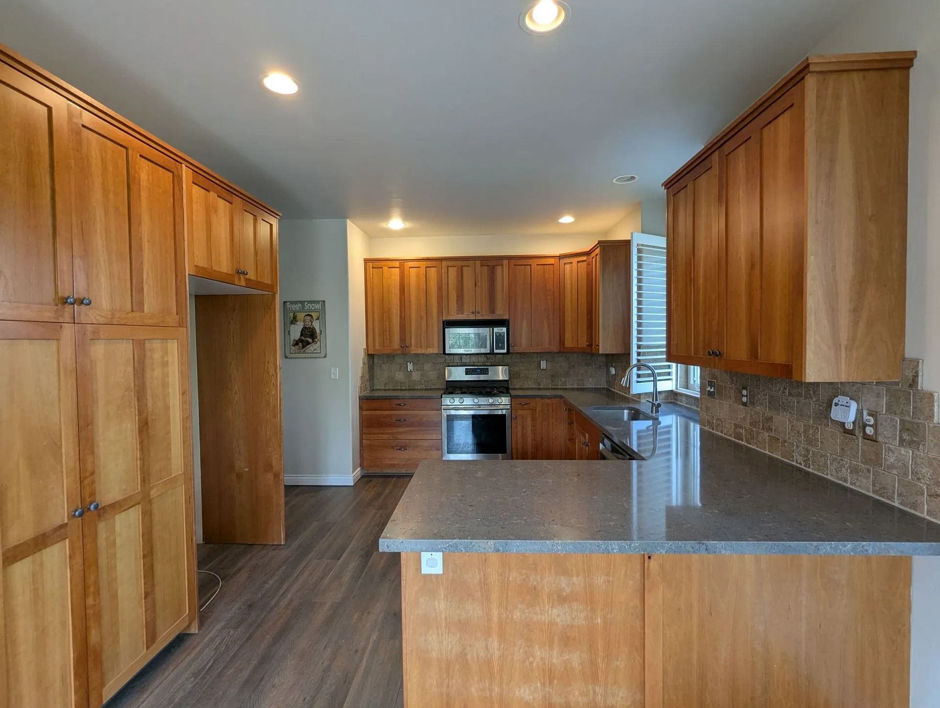 A kitchen featuring warm wood cabinetry, gray countertops, a stainless steel stove, and light wood-style flooring.
