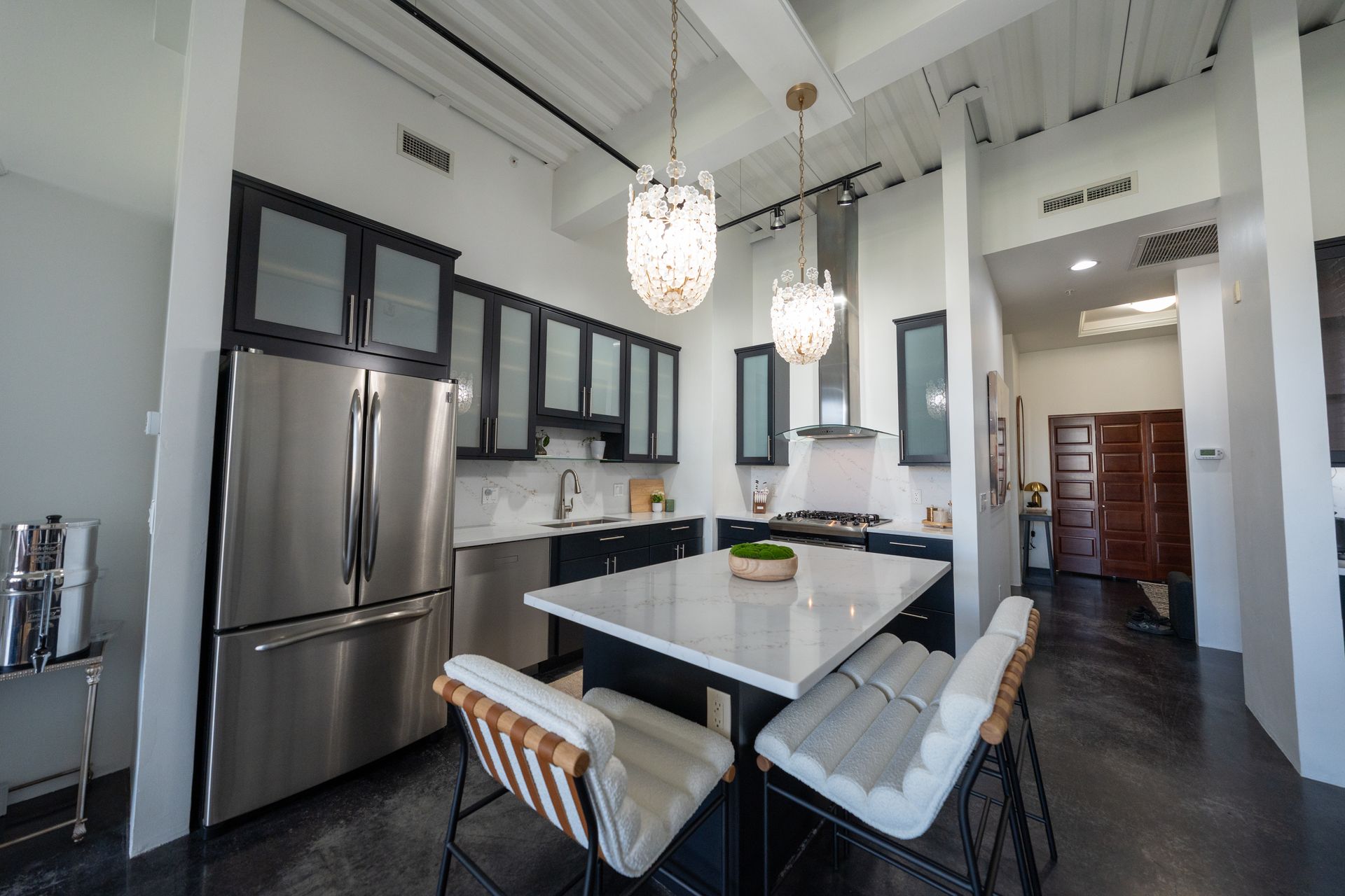Modern kitchen with stainless steel appliances, white island, black cabinets, and high ceiling chandelier