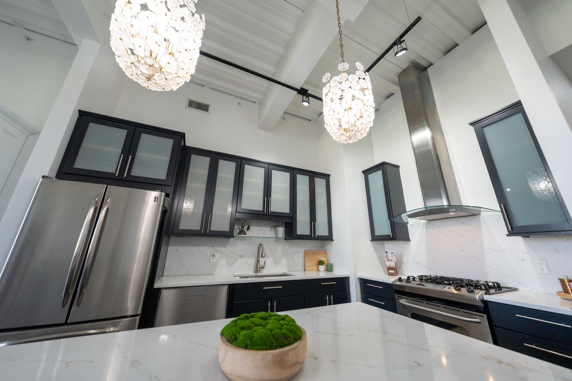 Modern white kitchen with stainless steel appliances, black cabinets, marble island, and pendant lights