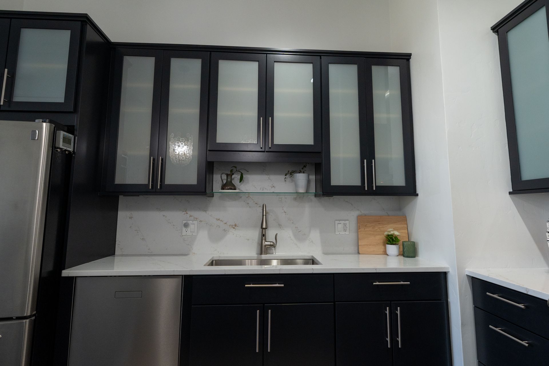 Modern kitchen with black cabinets, white countertops, stainless fridge, and sink under upper cabinets.