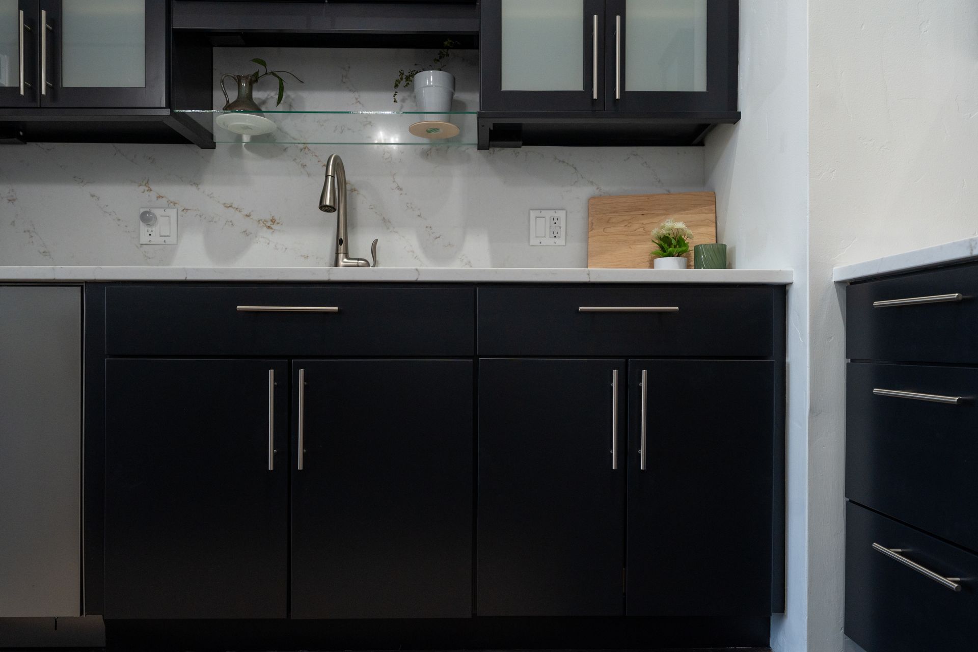 Modern kitchen with black cabinets, white countertop, sink, and marble backsplash