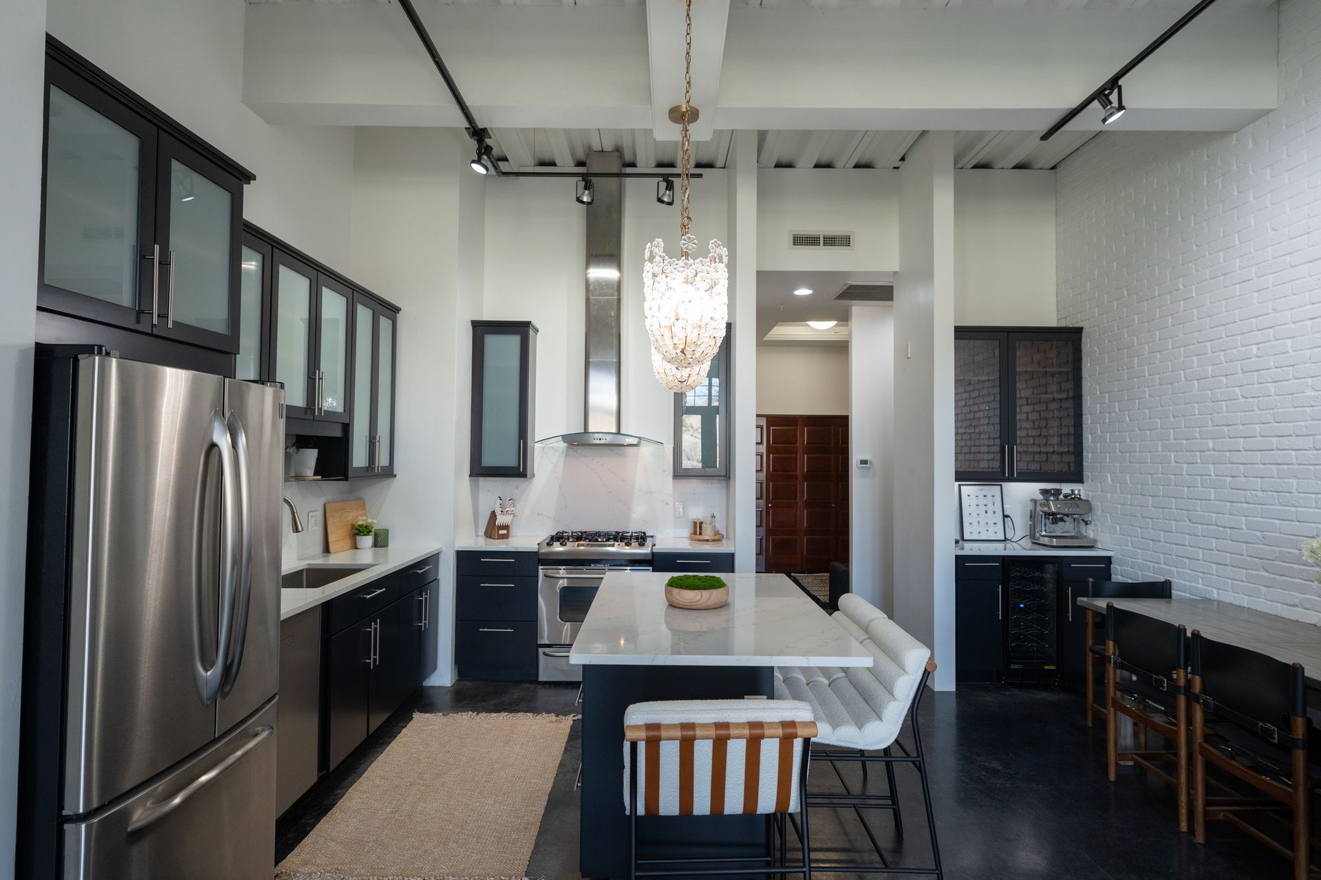 Modern open kitchen with stainless steel fridge, white island, black cabinets, and dining table