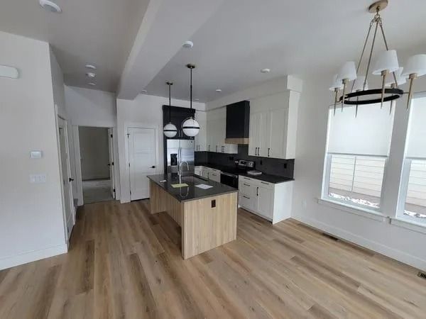 A modern kitchen with a wooden island, black countertops, white cabinets, and a chandelier over a light wood floor.
