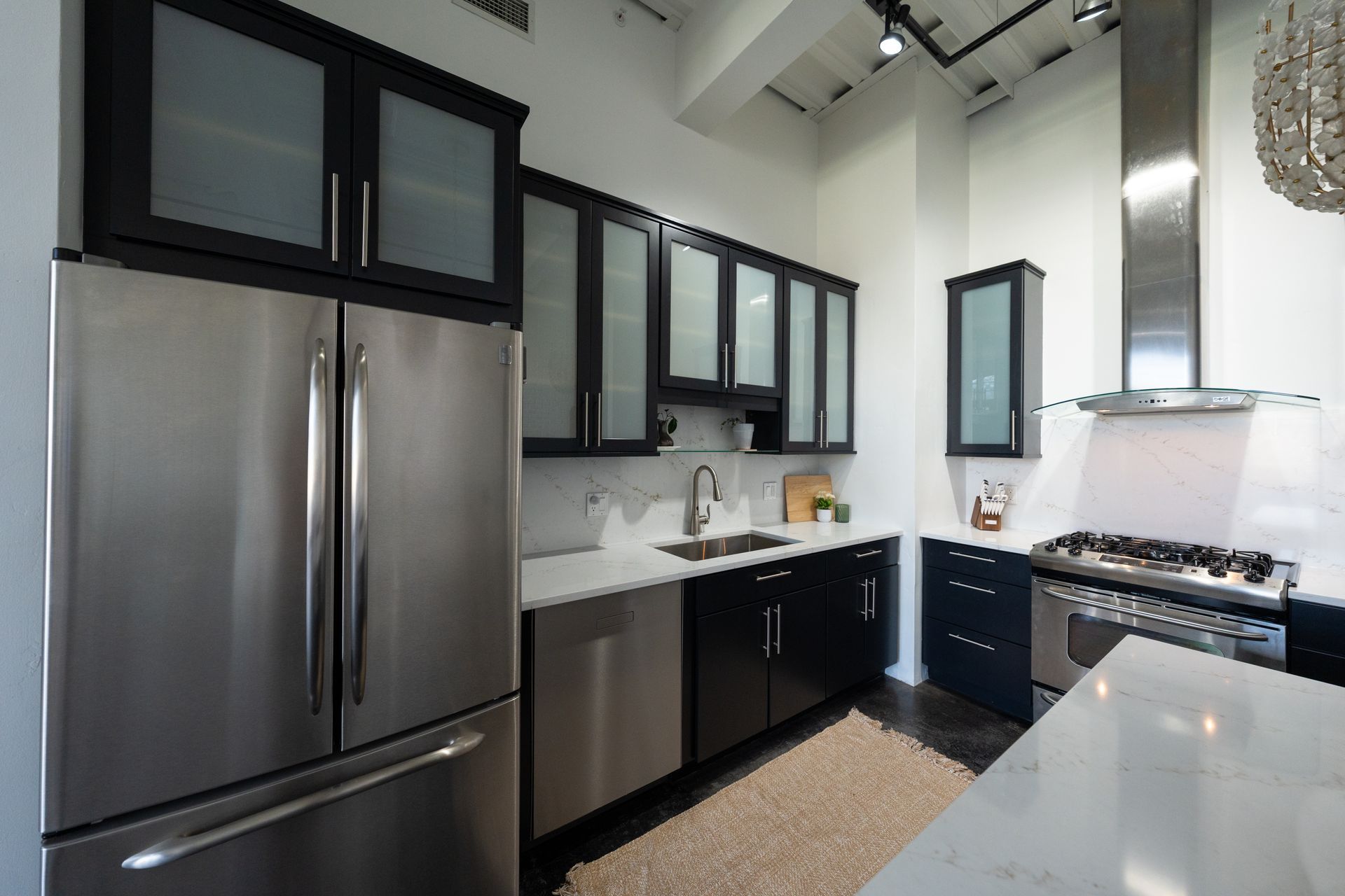 Modern kitchen with stainless steel refrigerator, black cabinets, white countertops, and large windows