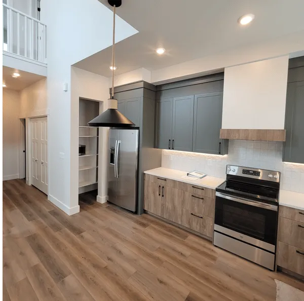 A kitchen with two-tone cabinetry featuring gray upper cabinets, wood-look lower cabinets, stainless appliances, and pantry.