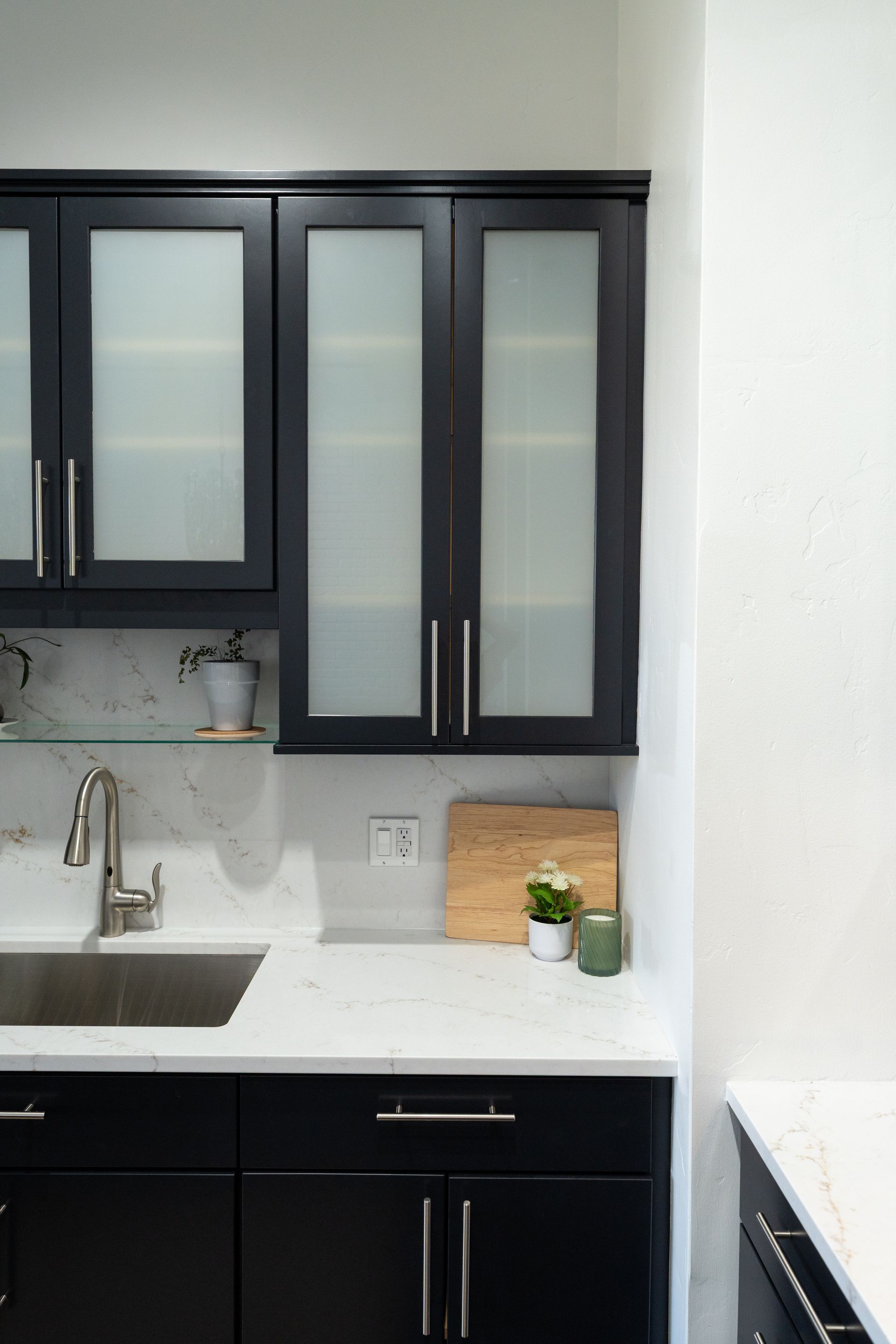 Modern kitchen with black cabinets, white countertops, stainless sink, and a small potted plant