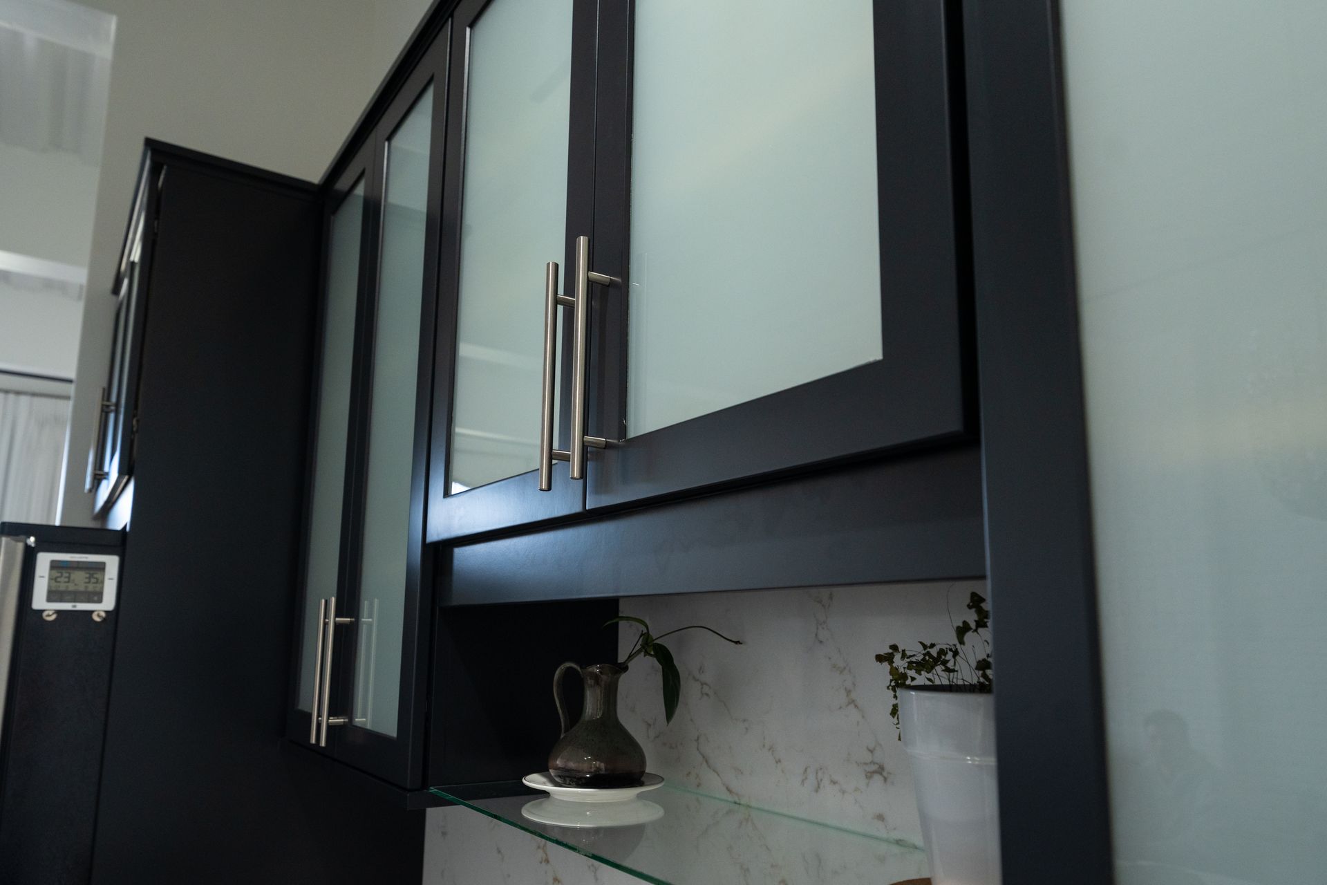 Black kitchen cabinets with frosted glass doors along a countertop and tiled backsplash