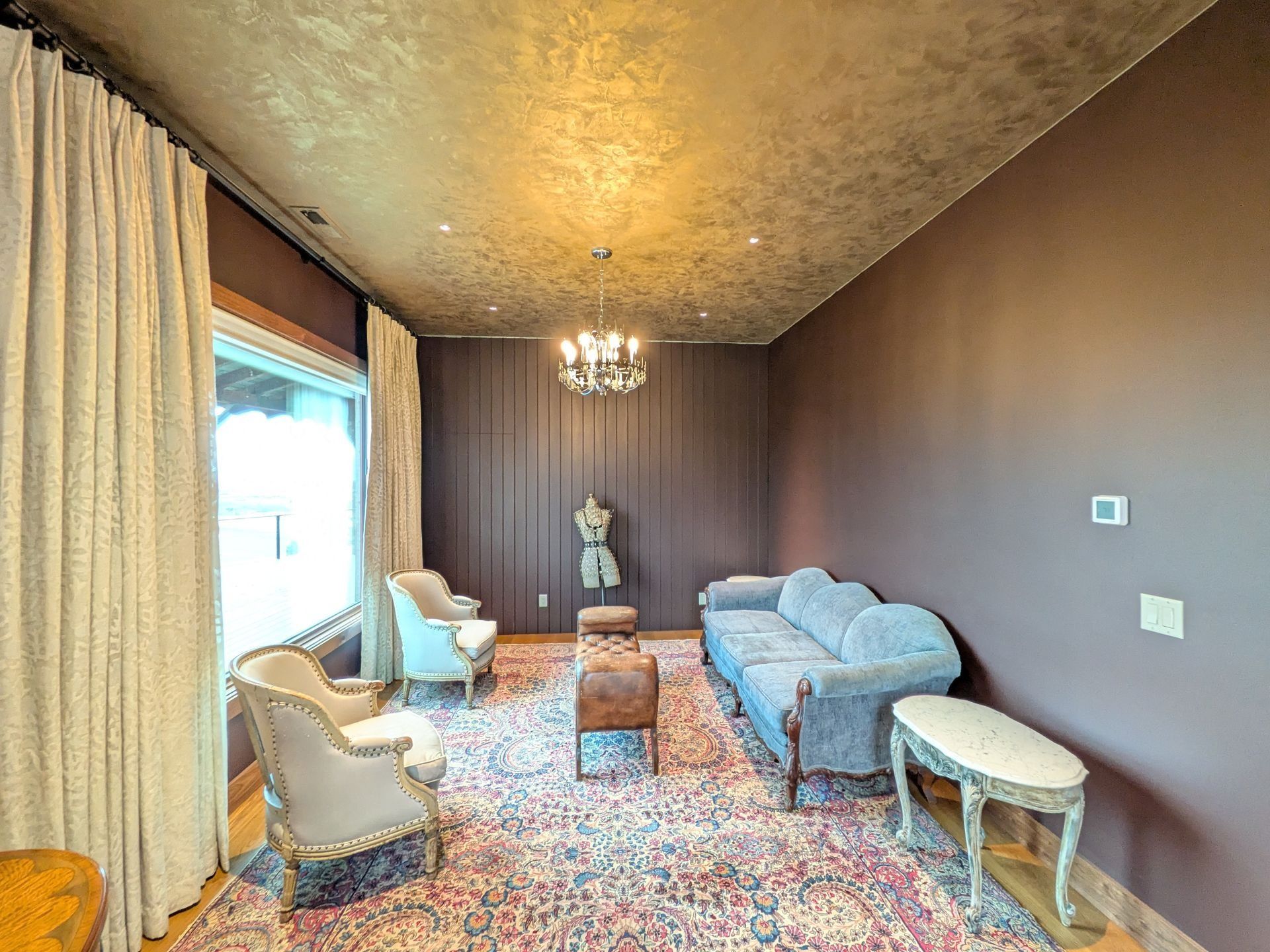 A cozy, dimly lit seating area with brown walls, a textured gold ceiling, a light blue sofa, two armchairs, and a rug.