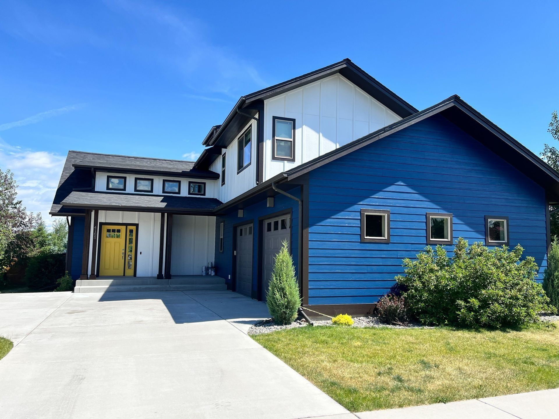 A two-story house with blue horizontal siding, white vertical siding, a yellow front door, and a concrete driveway.