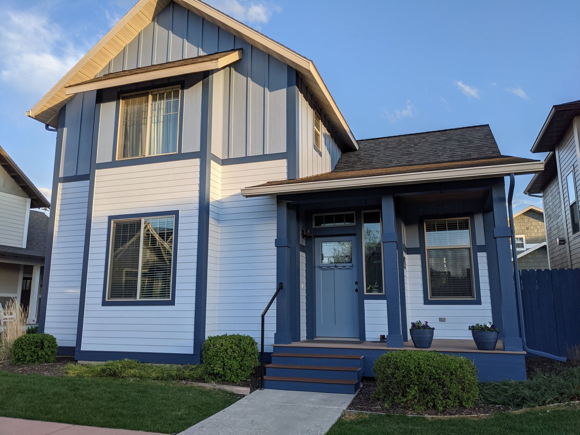 A two-story house with a light gray facade, blue trim, a covered porch, and a walkway leading to the front door.