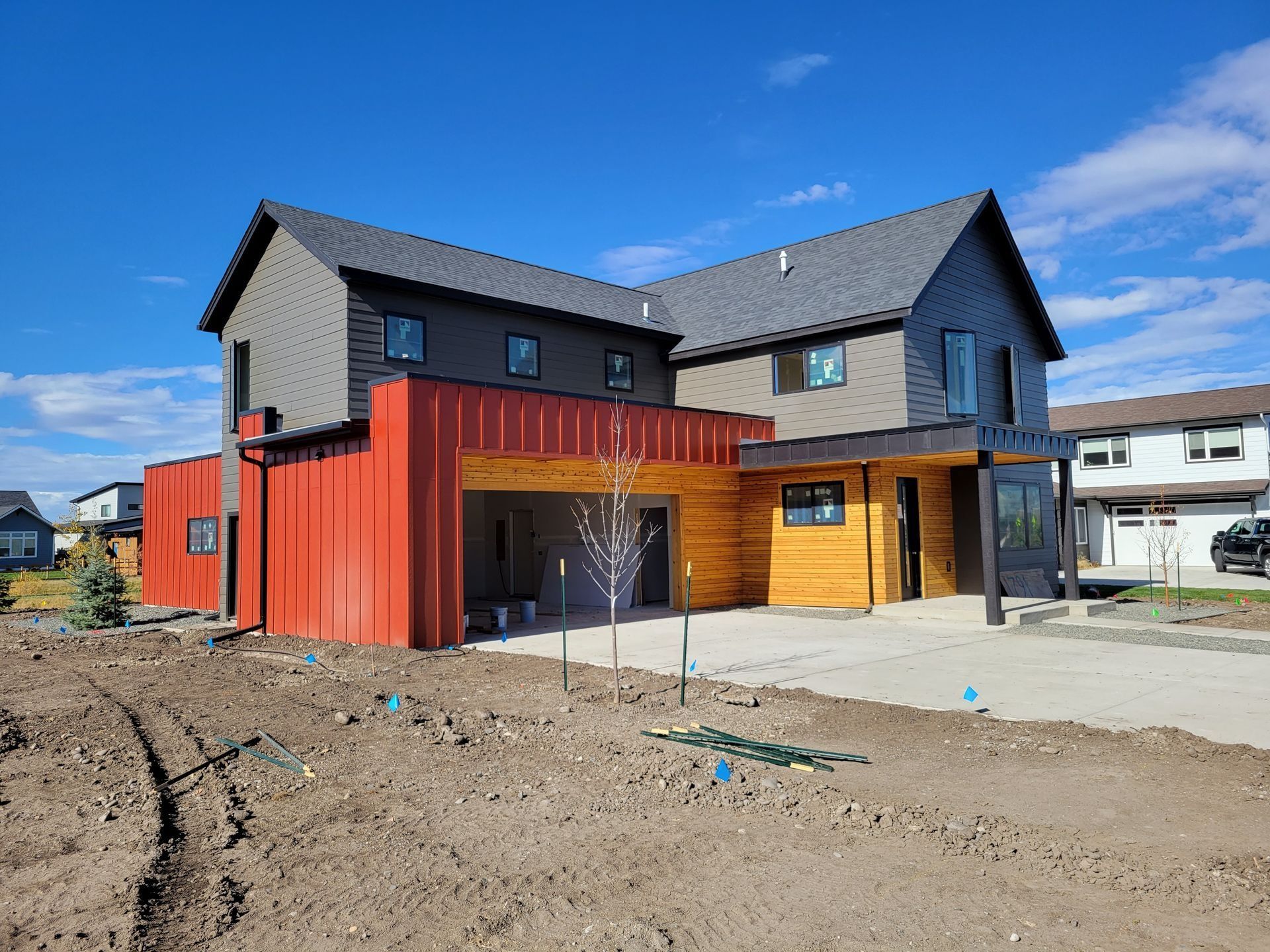A two-story home with gray siding, a red metal-clad entryway, and wood-paneled walls above a concrete driveway.