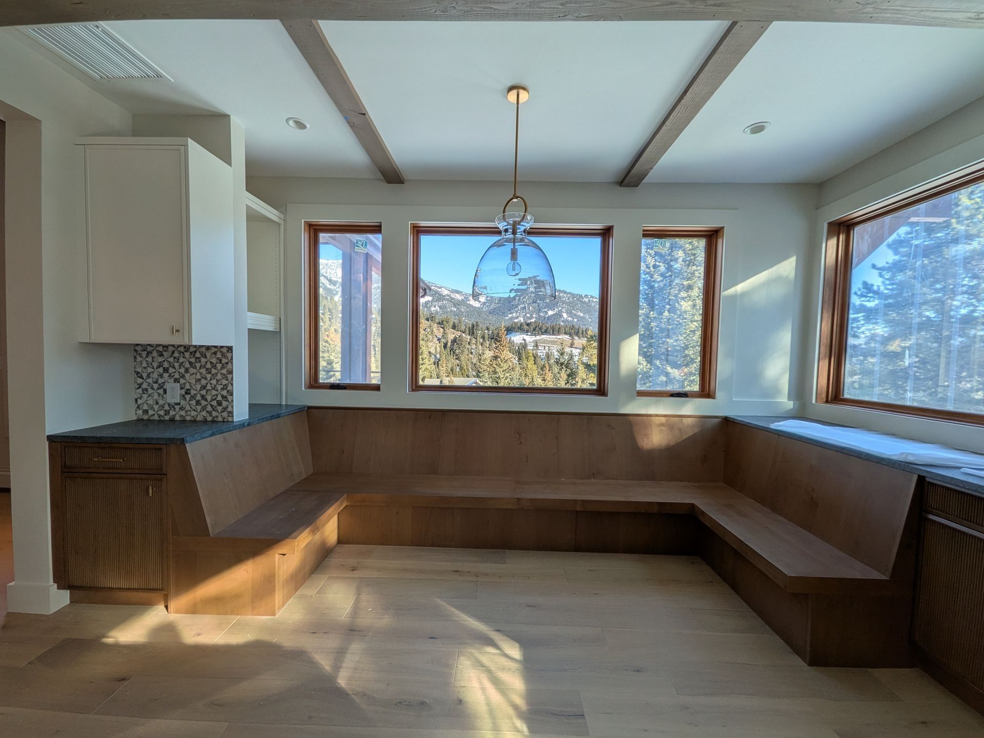 An L-shaped wooden built-in bench seating area with a pendant light, set against windows overlooking snowy mountains.