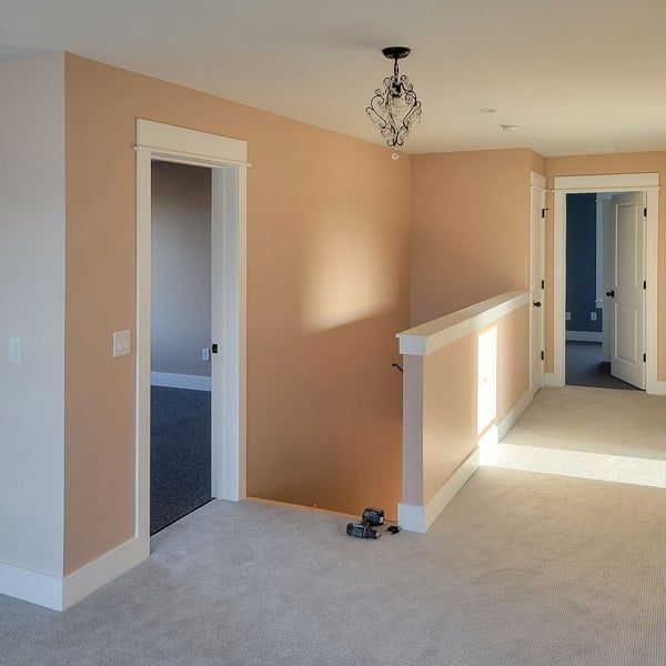 A second-floor hallway featuring beige walls, white trim, carpeted flooring, two open doorways, and a hanging light fixture.