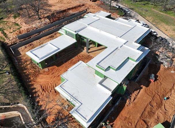 An aerial view of a construction site showing the white flat roof and green sheathed exterior walls of a new house.