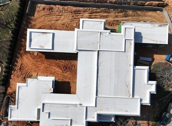 Aerial view of a white, flat-roofed building structure under construction on a dirt construction site.