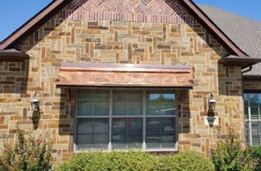 A window with a copper awning centered on a brick exterior wall with a herringbone brick pattern in the gable.