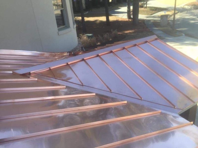 A high-angle view of a shiny copper standing seam metal roof meeting at a corner on a residential building.