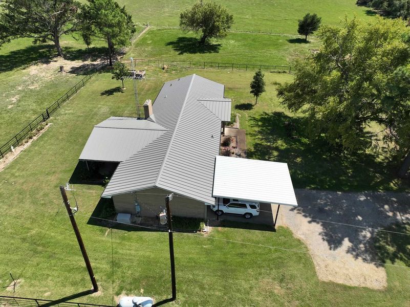 Aerial view of a gray-roofed house on a grassy property with a white carport sheltering a white vehicle.
