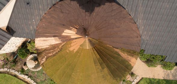 Aerial view of a circular, cone-shaped roof partially covered in sunlight, transitioning from deep brown to golden yellow.