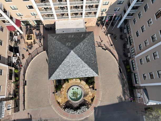 Aerial view of an urban courtyard with a central fountain and a square, dark-tiled roof structure, flanked by buildings.