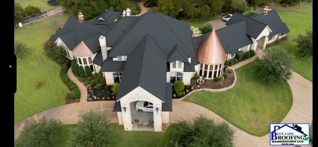 Aerial view of a large luxury home with dark gray roof tiles and copper-accented turrets, surrounded by green lawns.